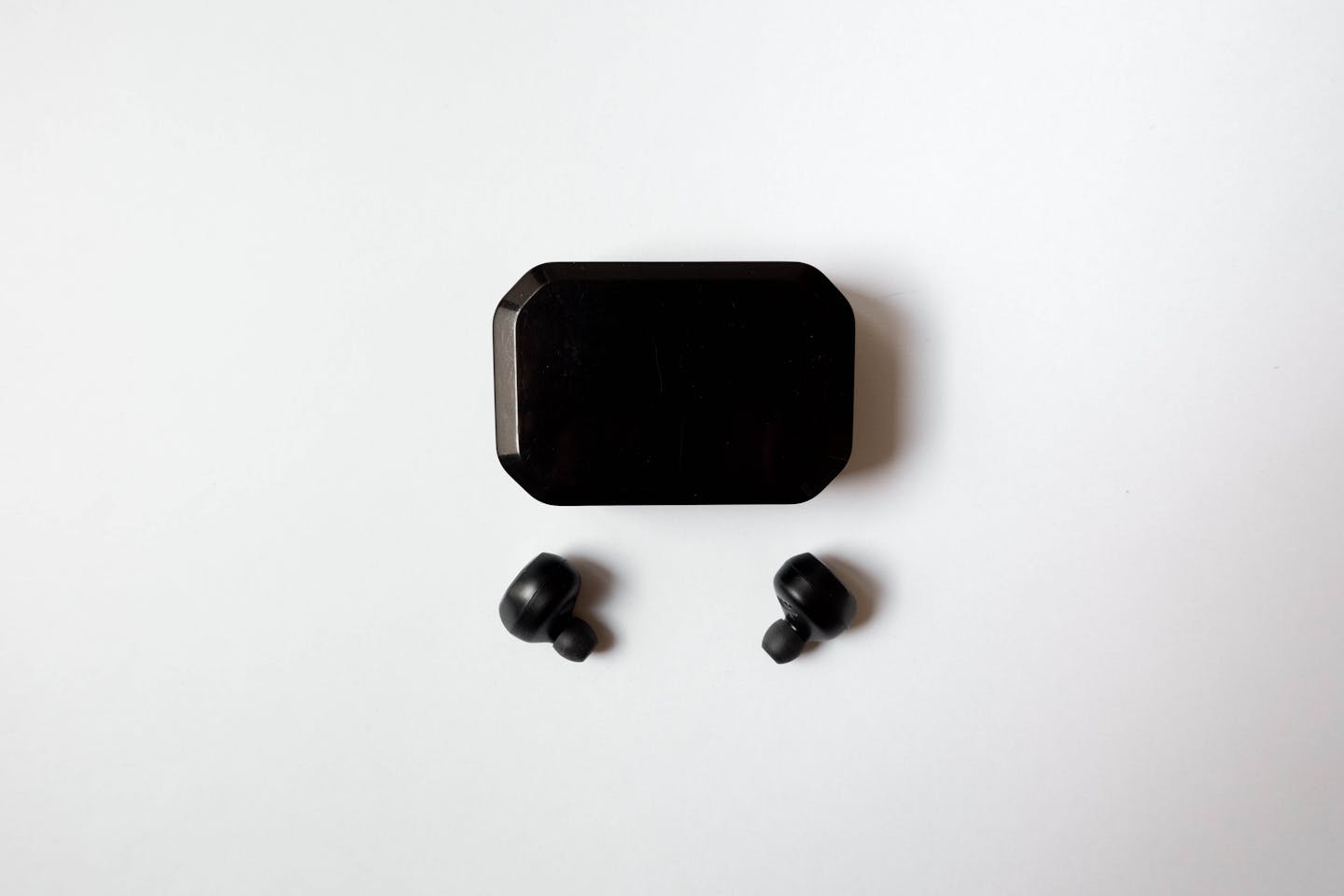 Black wireless earbuds with charging case flat-lay on white background